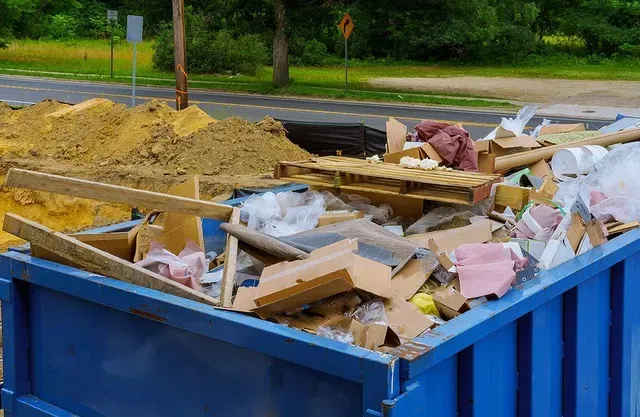 A blue dumpster filled with cardboard , plastic , and wood.