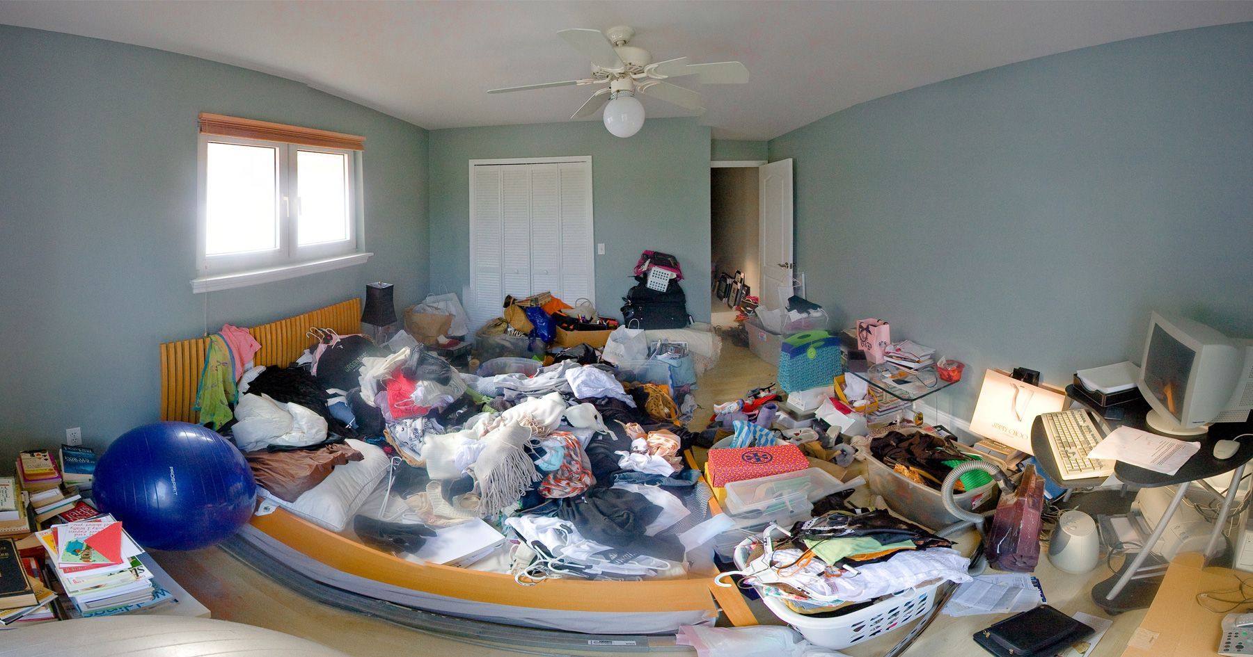 A bedroom with a lot of stuff on the floor and a ceiling fan.