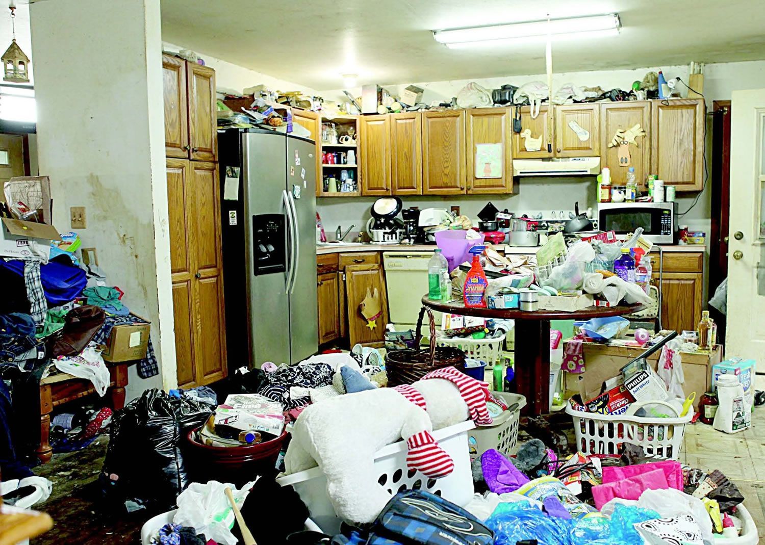 A very messy kitchen with a lot of clothes on the floor.