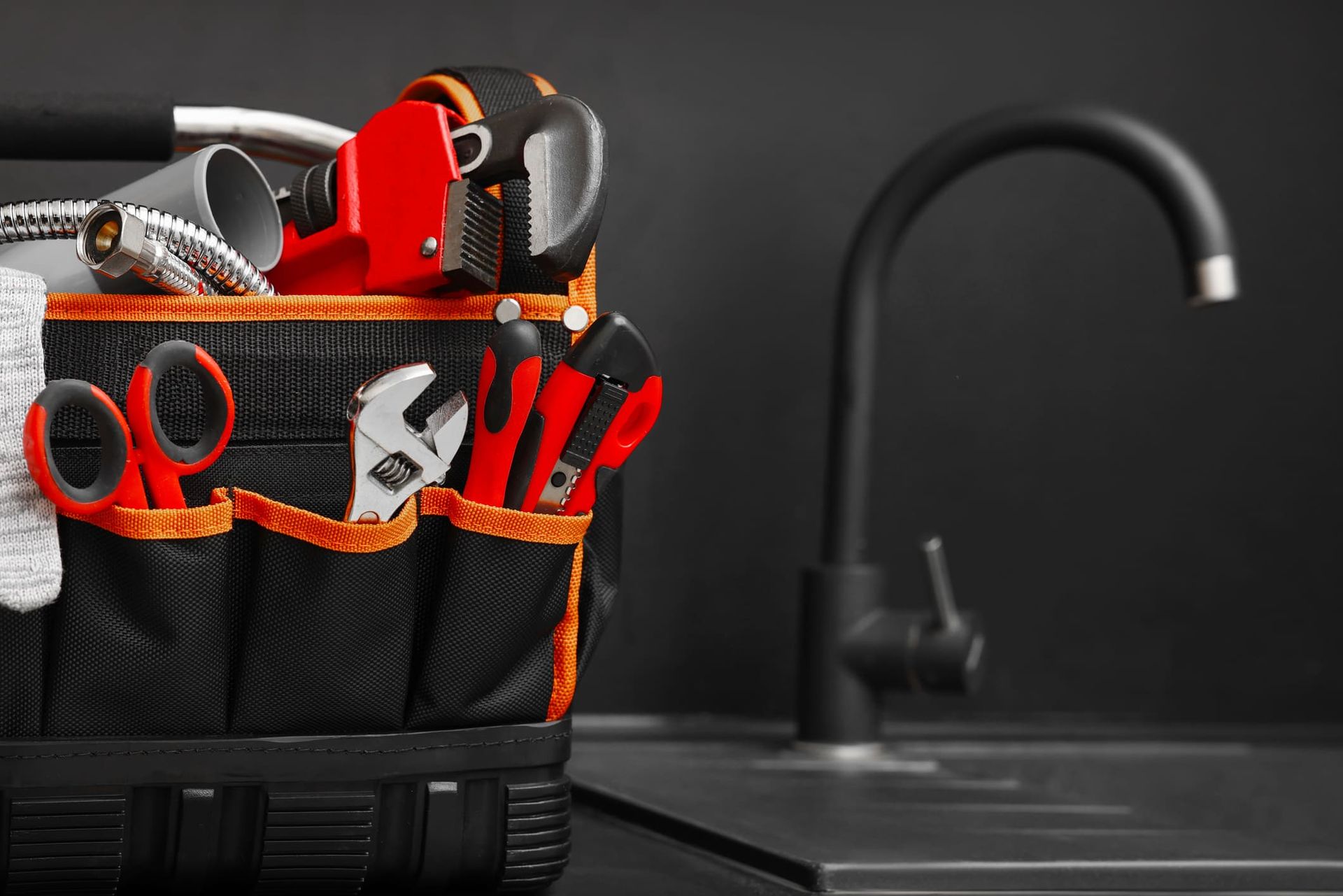 A tool bag filled with tools is sitting on a counter next to a sink.