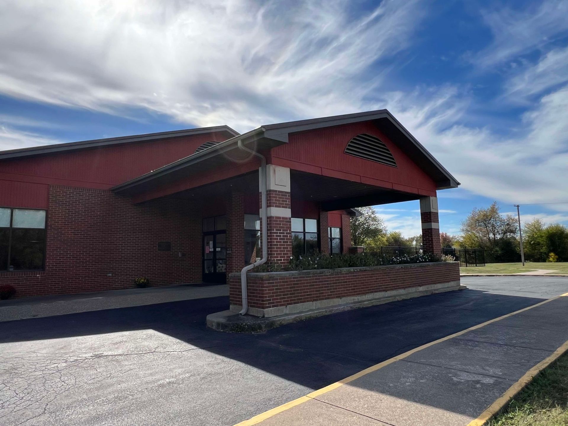 A red brick building with a porch and a parking lot in front of it.