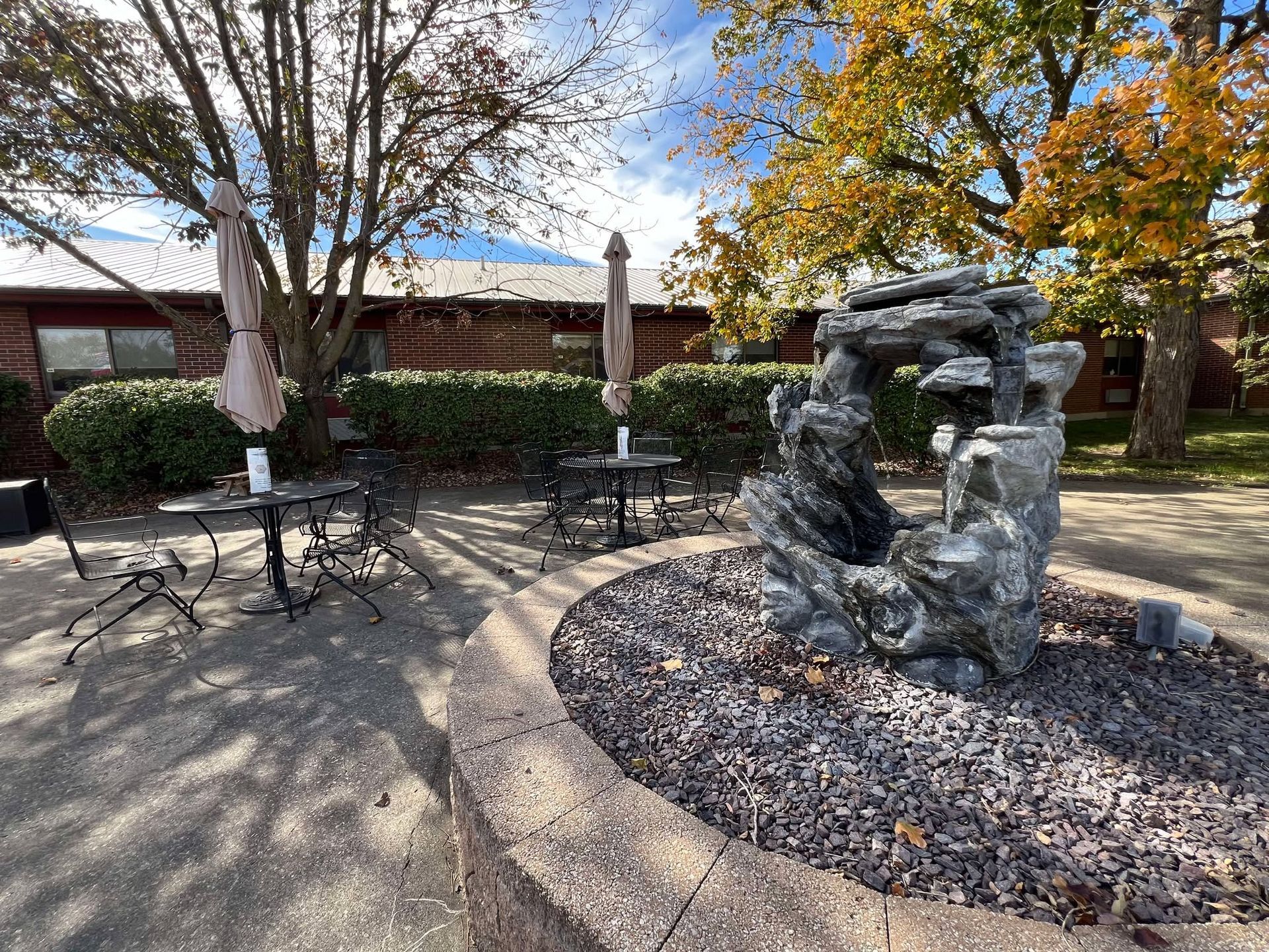 There is a fountain in the middle of the patio with tables and chairs.