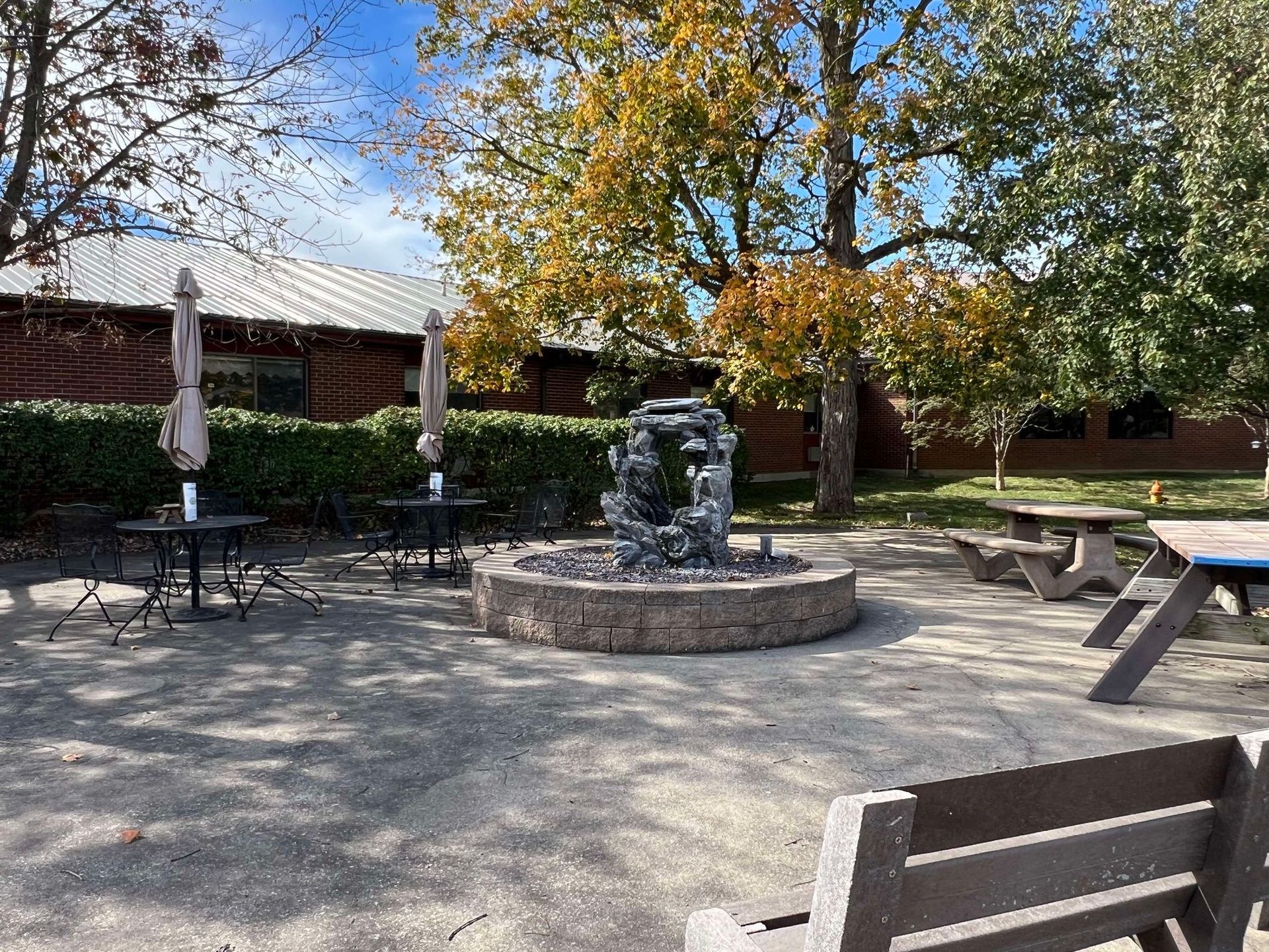 There is a fountain in the middle of the courtyard with tables and benches.