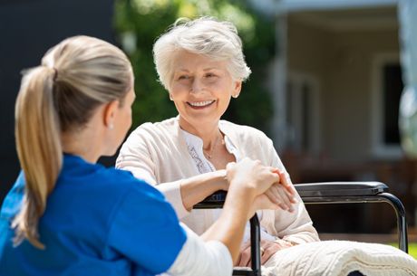 A nurse is holding the hand of an elderly woman in a wheelchair.