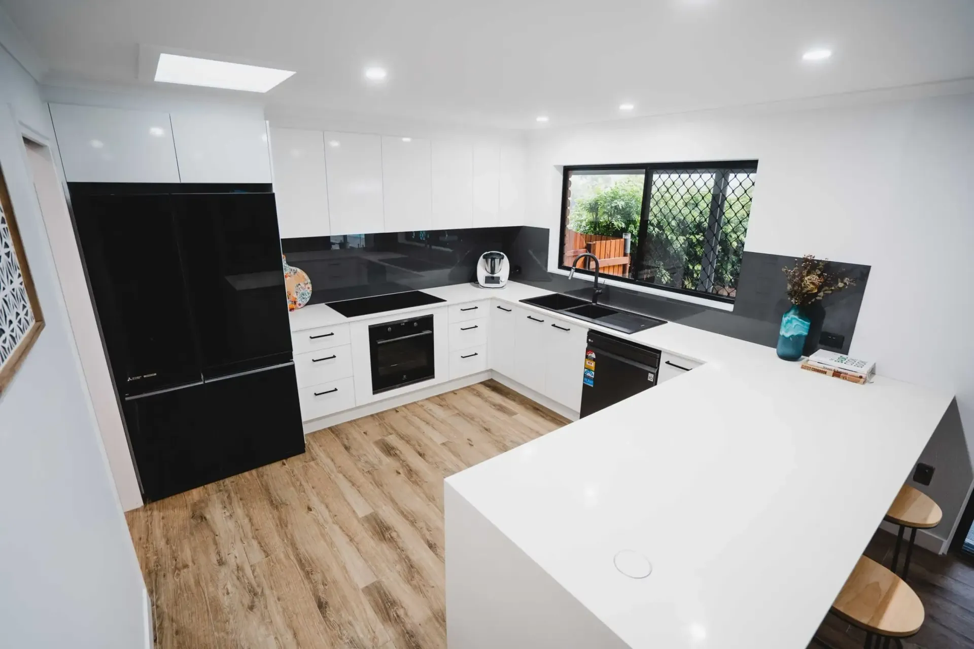 Modern white kitchen with black appliances, island, and wood flooring — CK Cabinetry in Coolum Beach, QLD