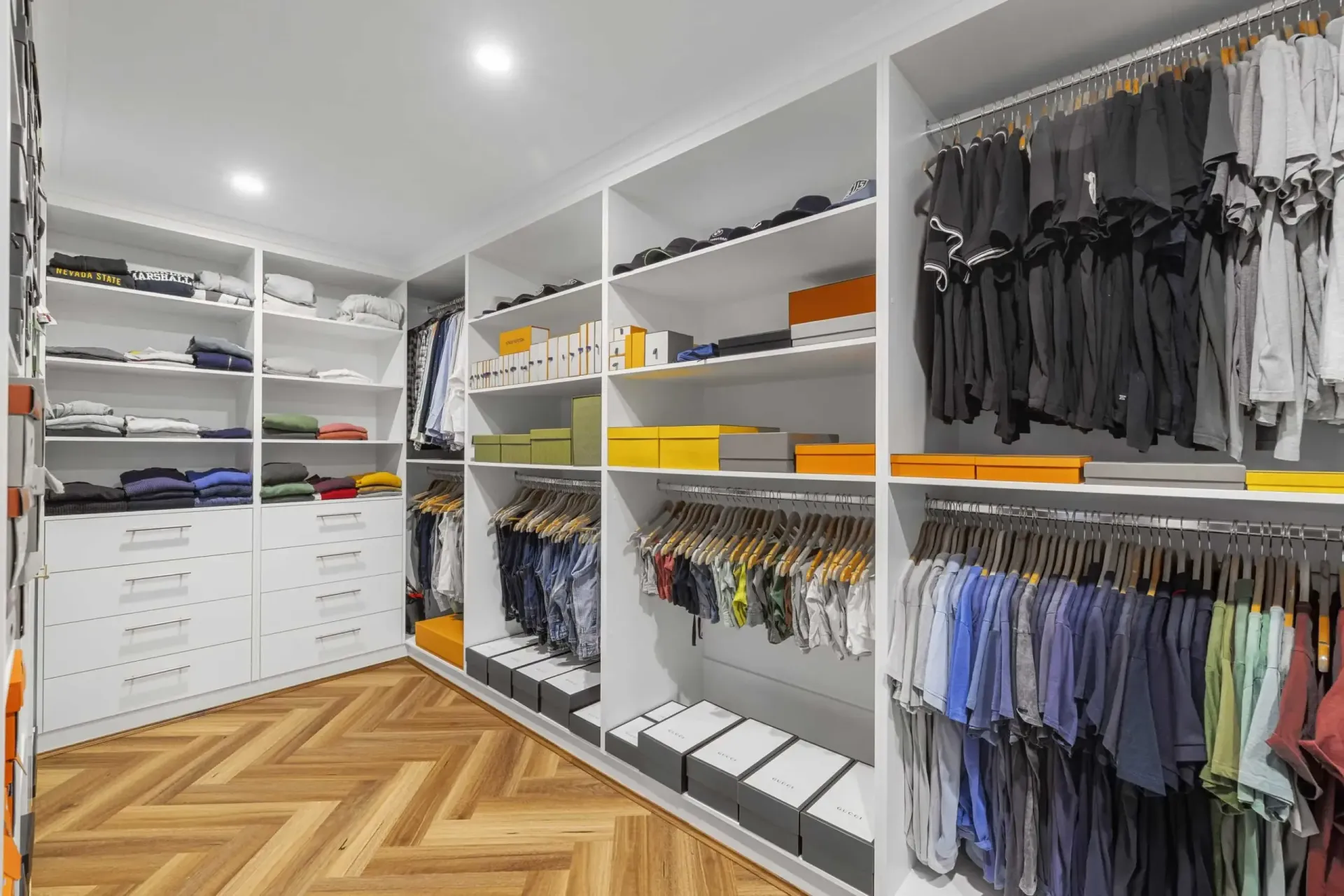 Walk-in closet with white shelves and hanging clothes, organized with boxes and a herringbone wood floor — CK Cabinetry in Coolum Beach, QLD