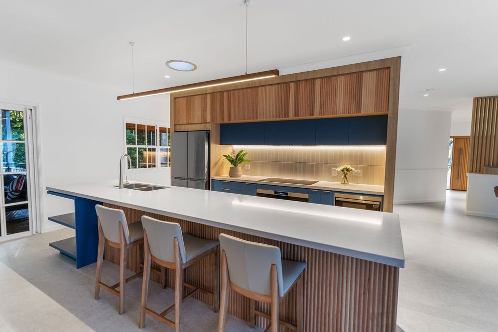 Modern kitchen with large island, bar stools, timber cabinetry, blue accents and sleek lighting.
