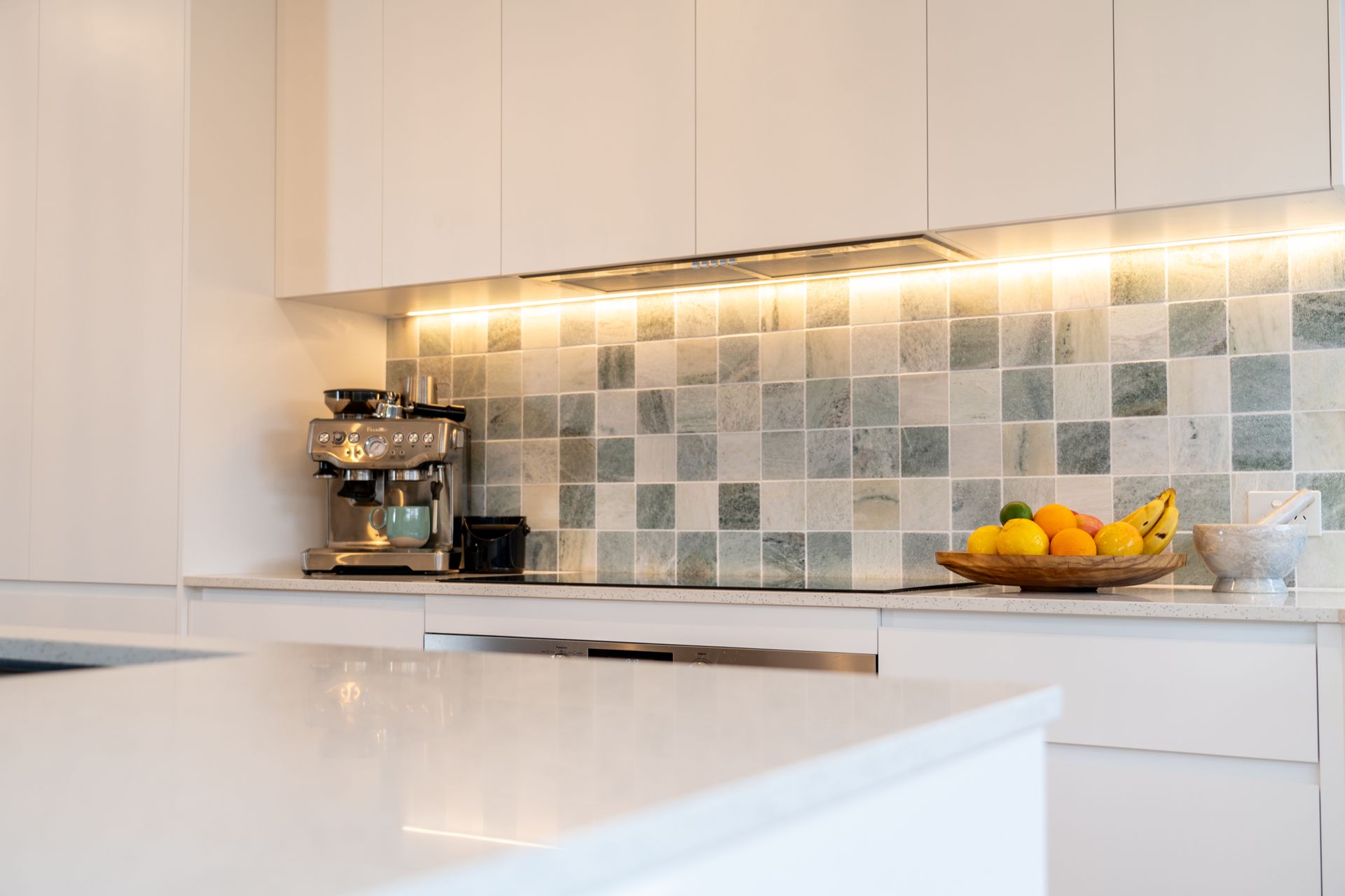 White kitchen with marble backsplash, espresso machine, fruit basket, and under-cabinet lighting — CK Cabinetry in Coolum Beach, QLD