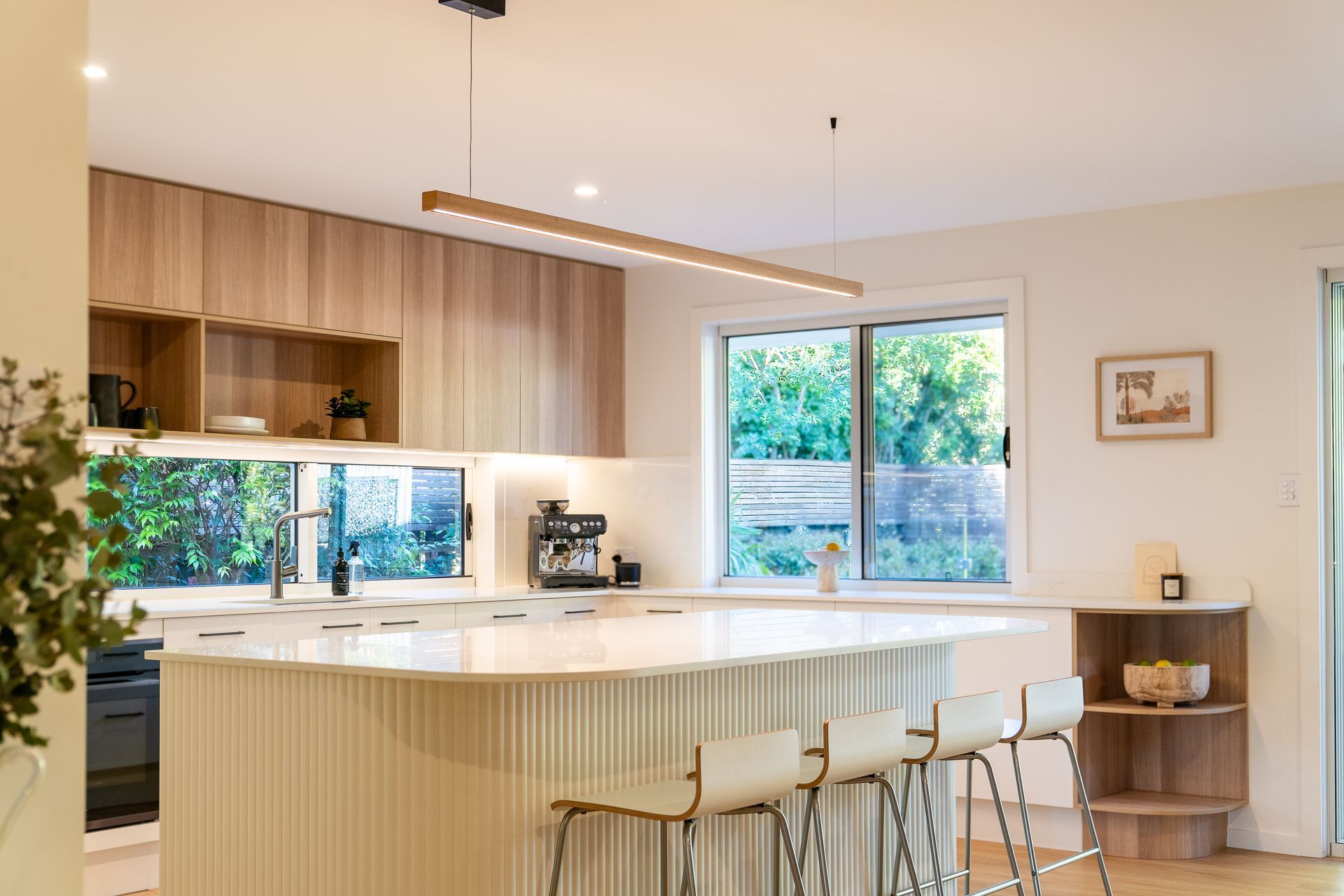 Modern kitchen with light wood cabinets, white island with bar stools, and large window — CK Cabinetry in Coolum Beach, QLD
