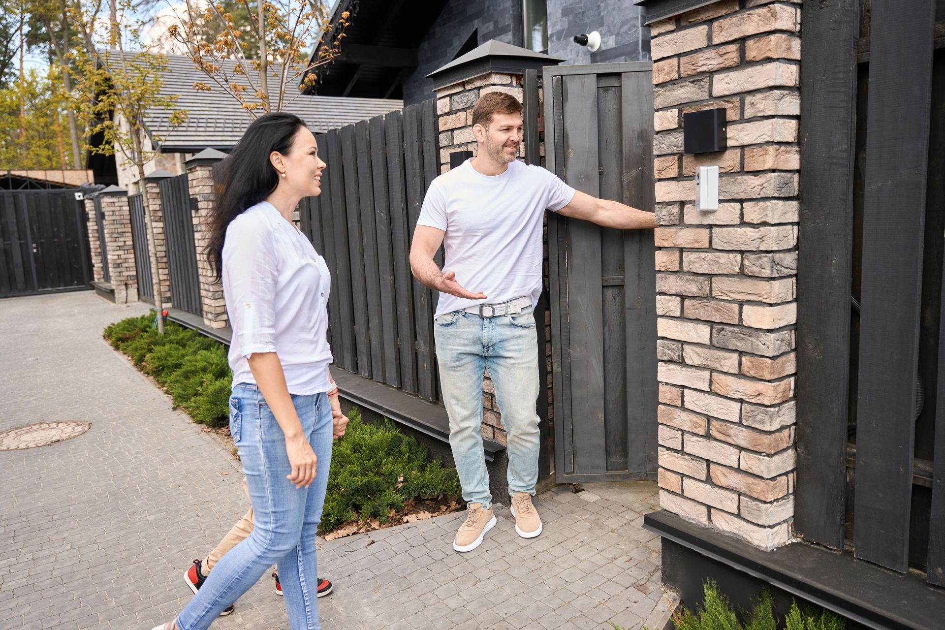 Man opening gate for a woman; they smile and are outside near a brick pillar and fence.