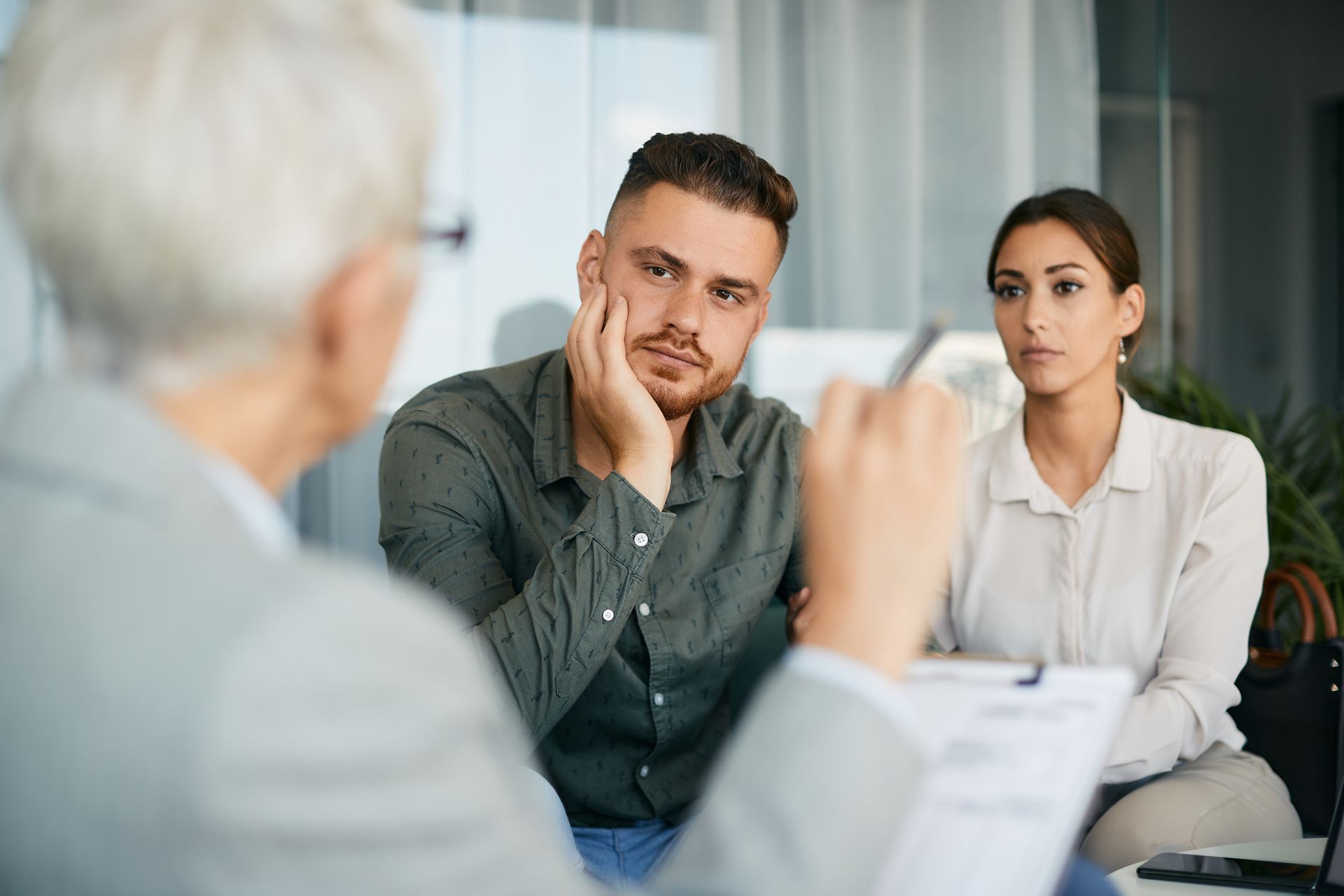 Couple in a counseling session, listening attentively. Neutral indoor setting.