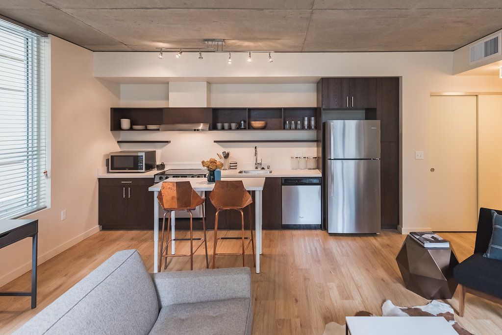 A living room with a couch and a kitchen with a stainless steel refrigerator.