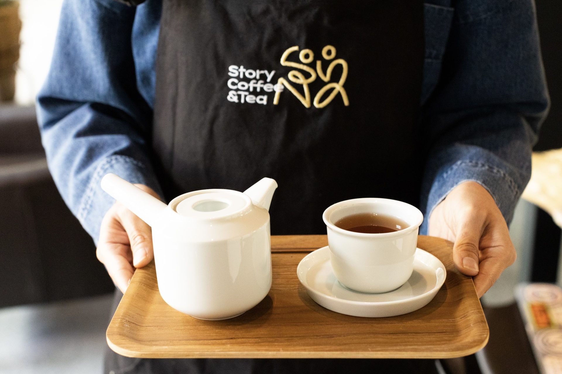 A person is holding a tray with a teapot and cup of tea on it.