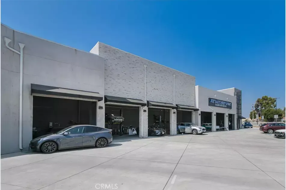 Gray Tesla parked outside a commercial building with open garage bays, under a clear blue sky.