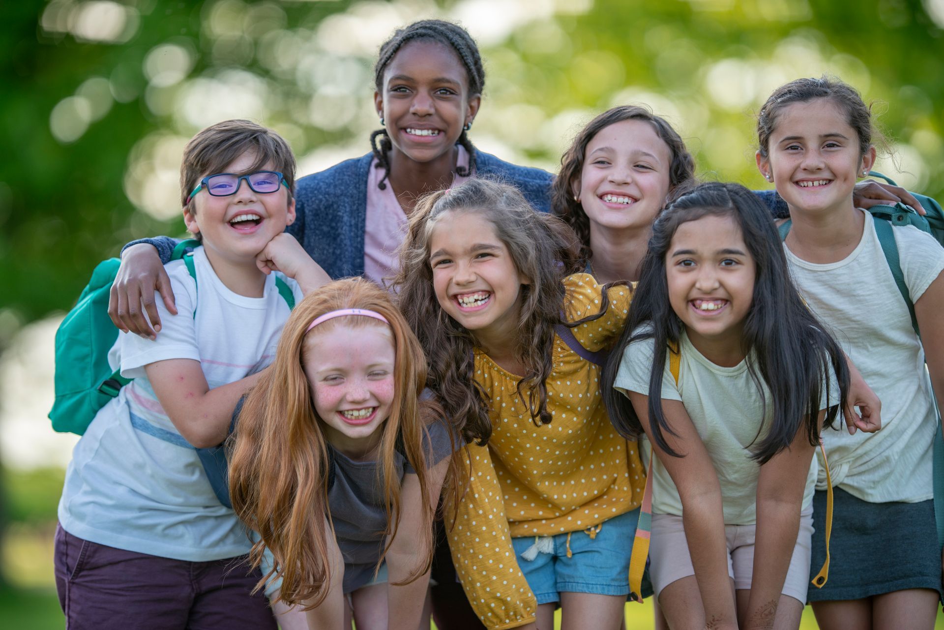 Group of smiling children, embracing, outside.