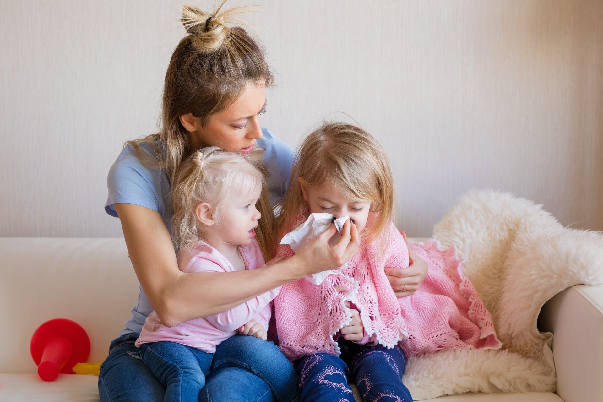 Mom wiping the nose of her young daughter while holding a toddler