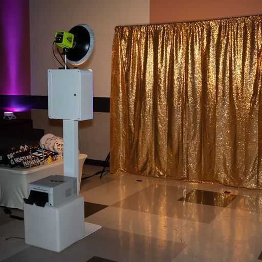 White photo booth machine beside a gold curtain in an indoor event space with purple accent lighting