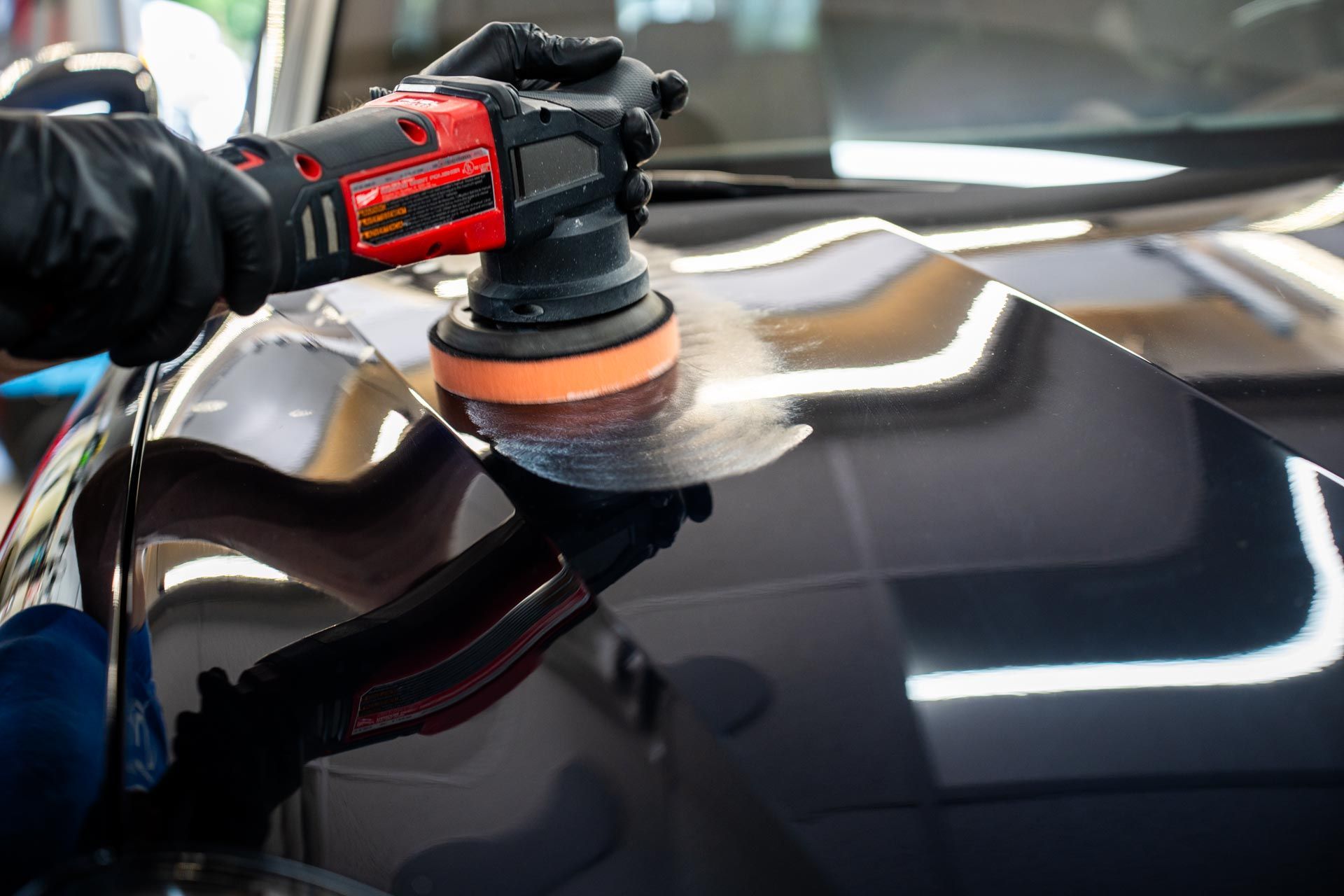 A person is polishing the hood of a car with a machine.