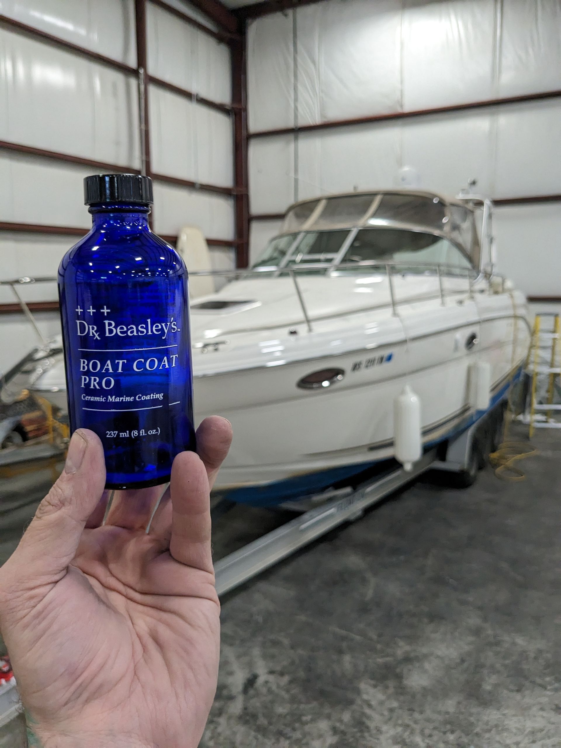 A person is holding a blue bottle in front of a boat