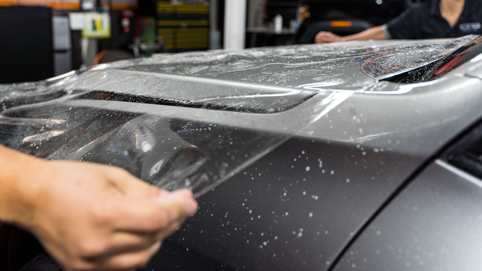 A person is applying a protective film to the hood of a car.