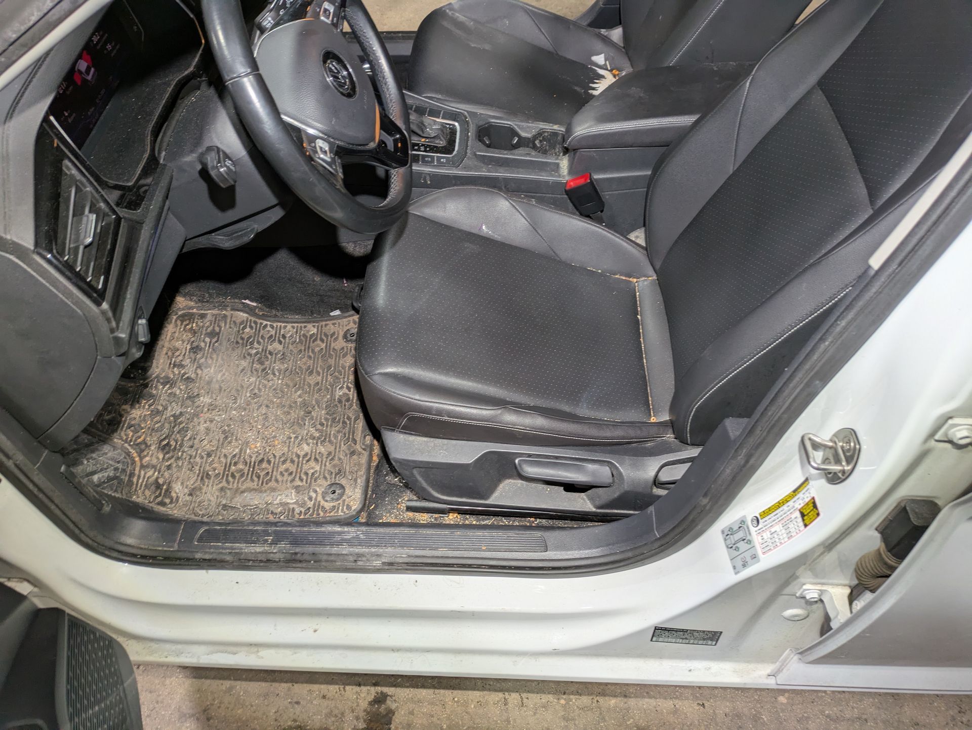 The inside of a white car with the door open and dirty seats.