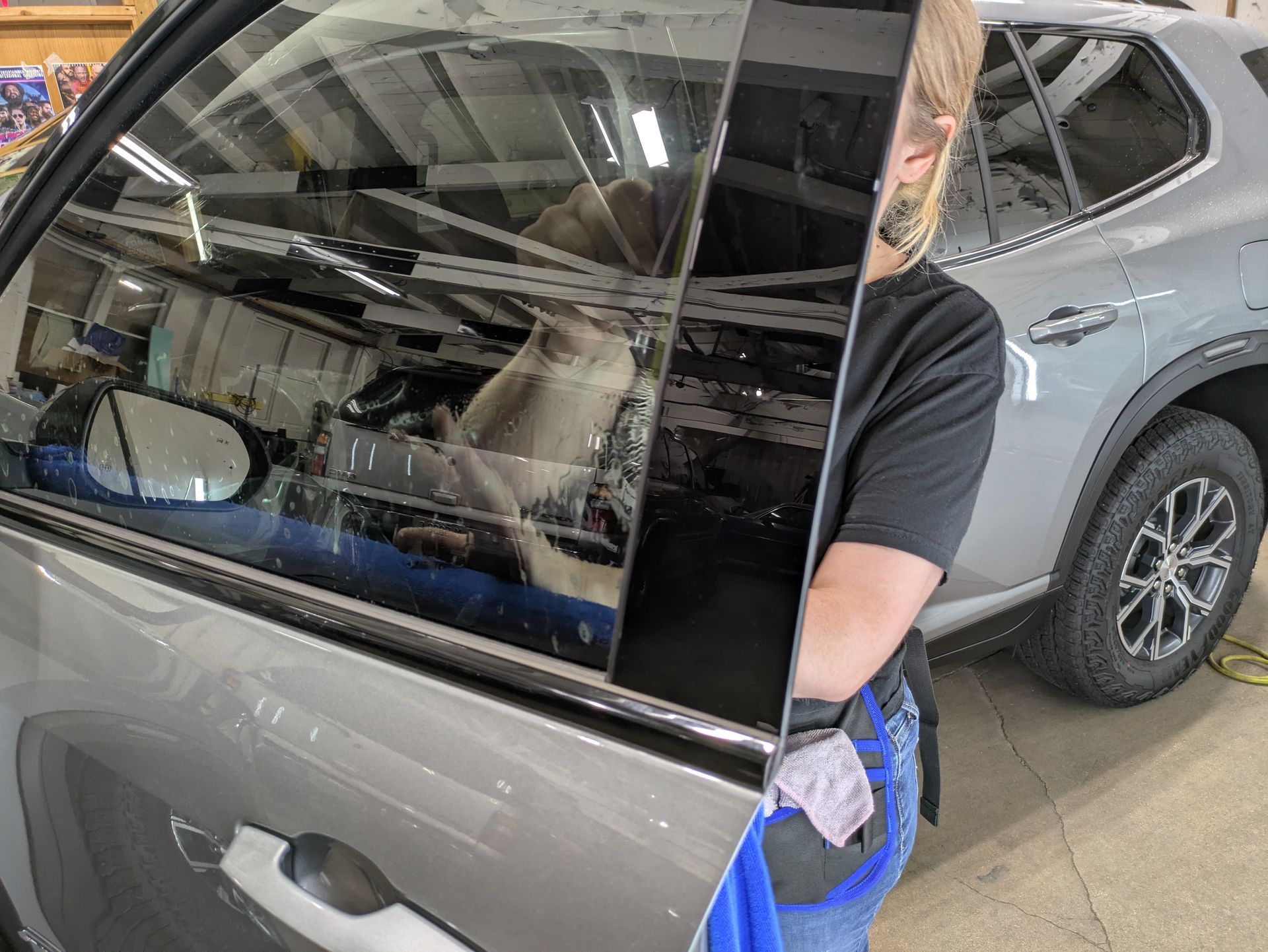 A woman is cleaning the windows of a car in a garage.