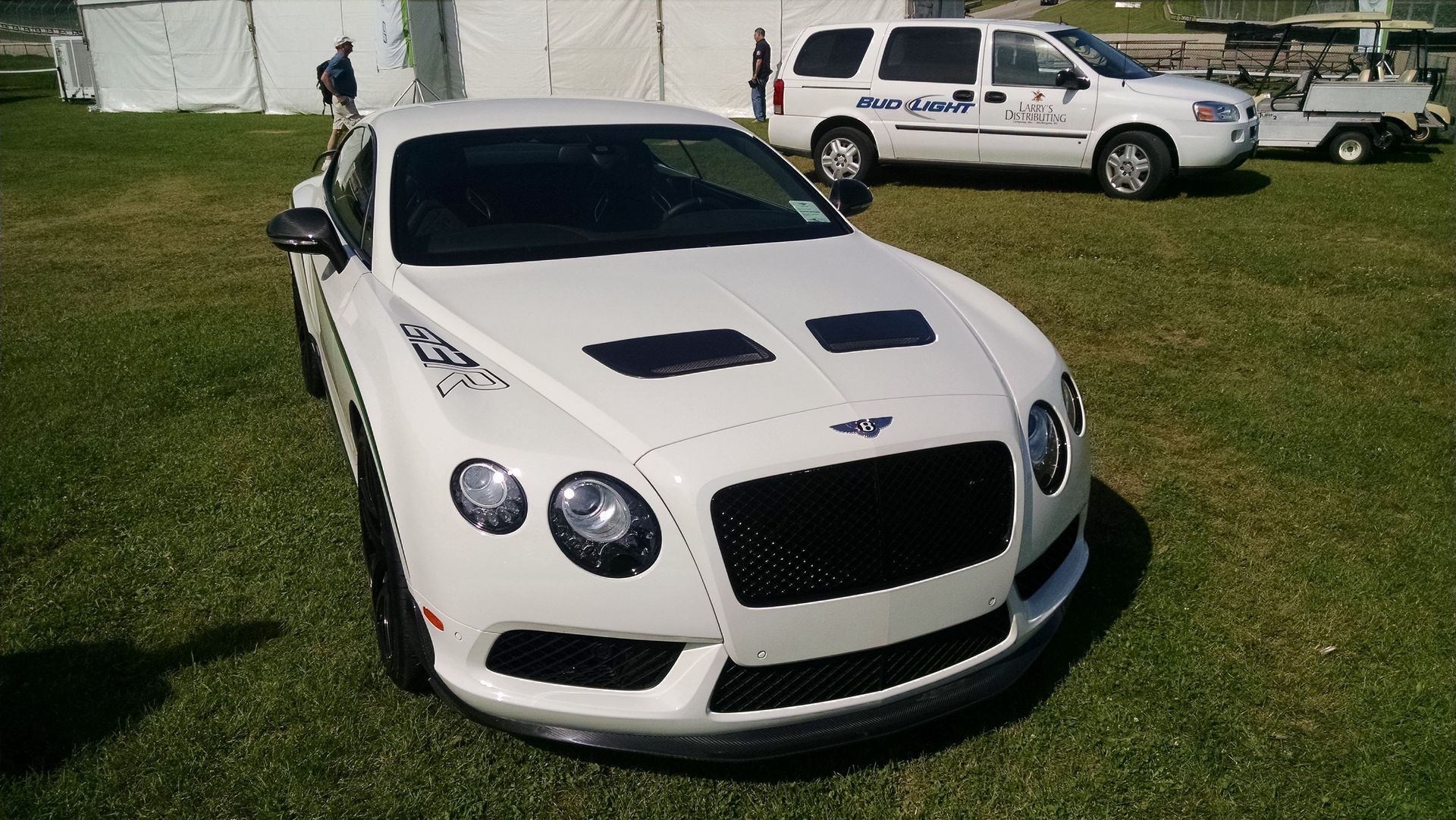 A white bentley is parked in a grassy field