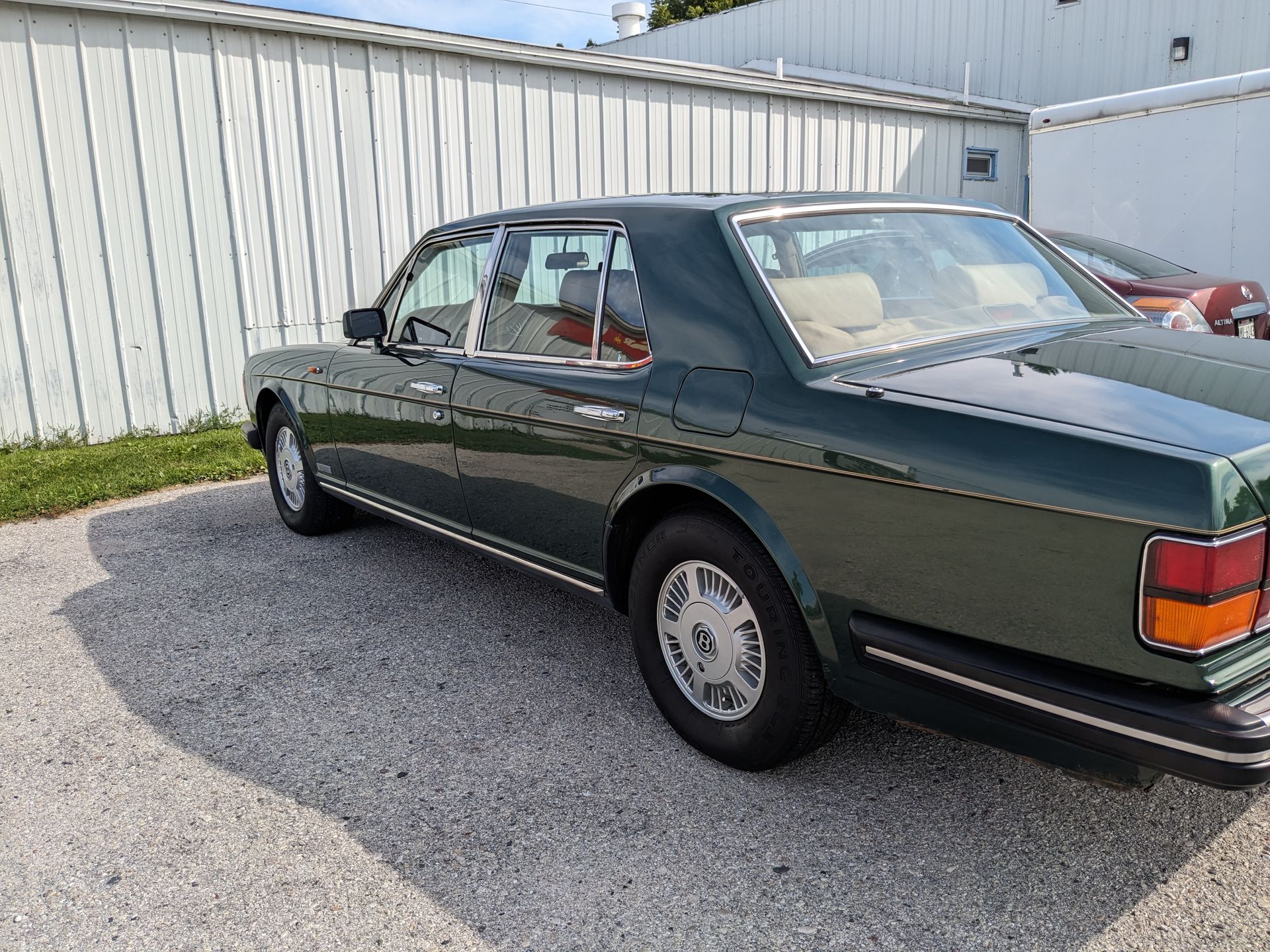 A green car is parked in front of a white building.
