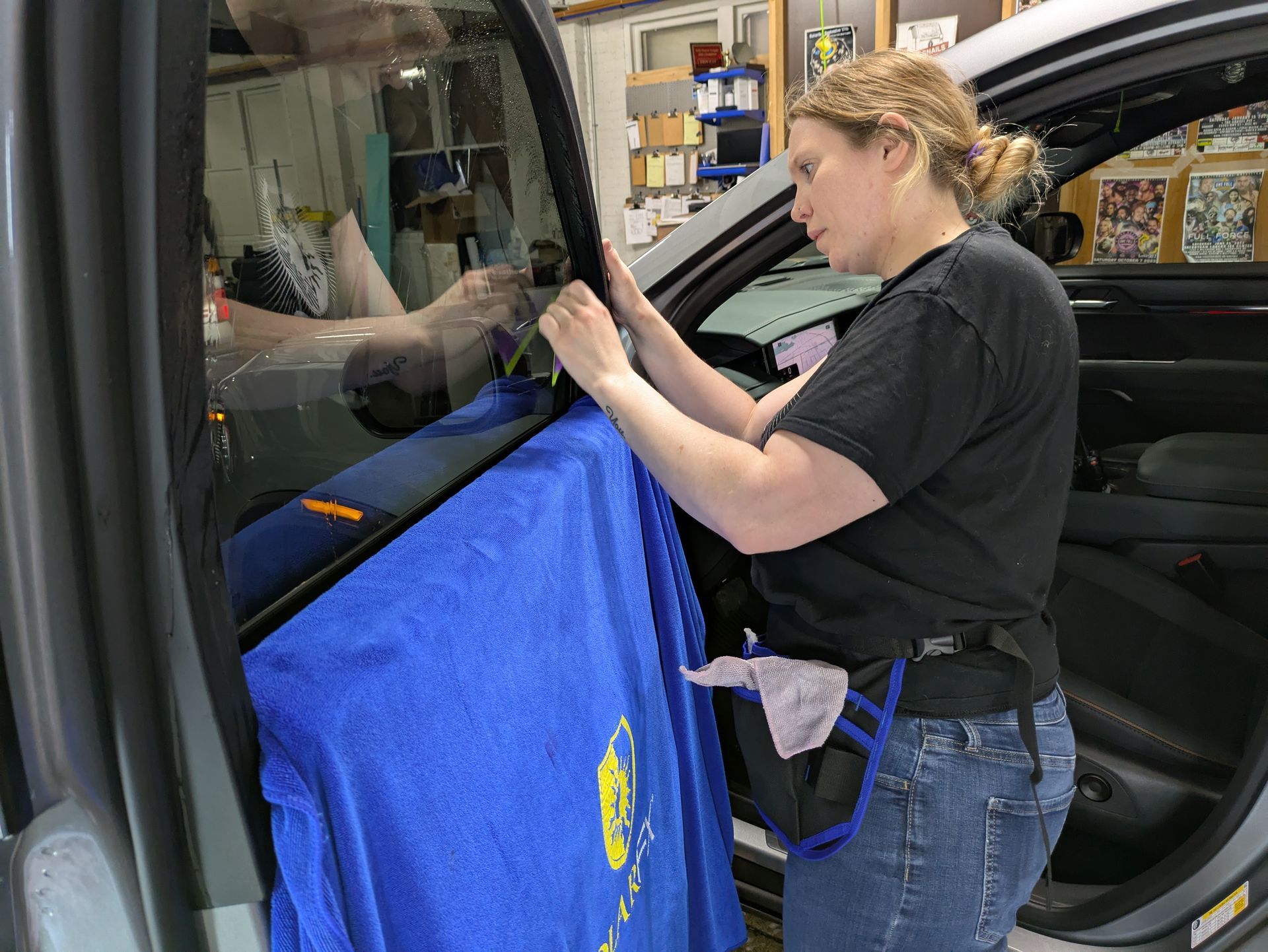 A woman in a black shirt is working on a car window.