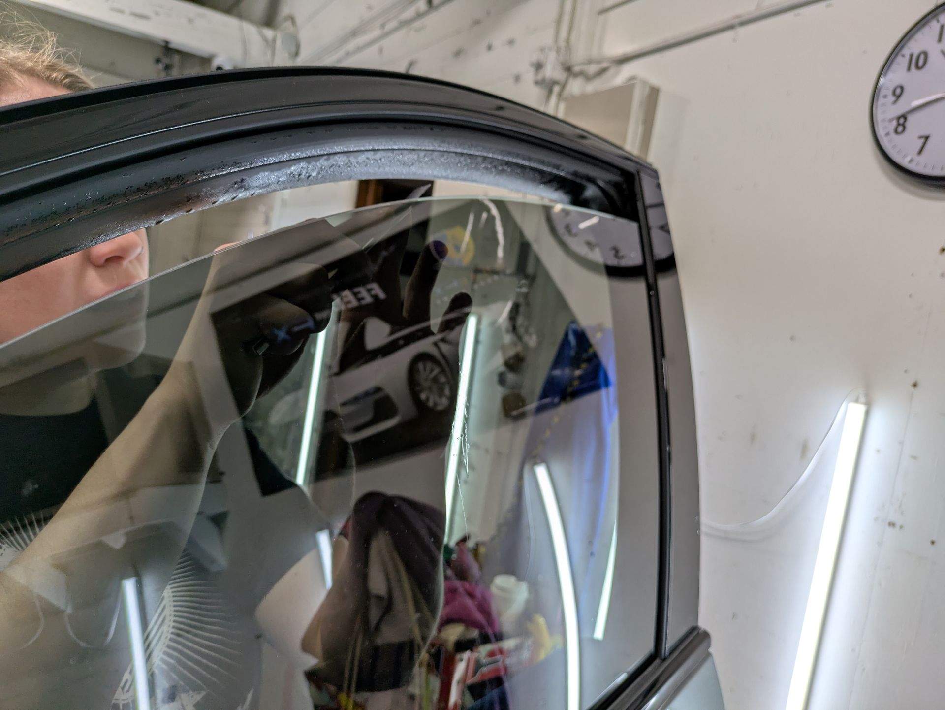 A man is looking through a car window in a garage.