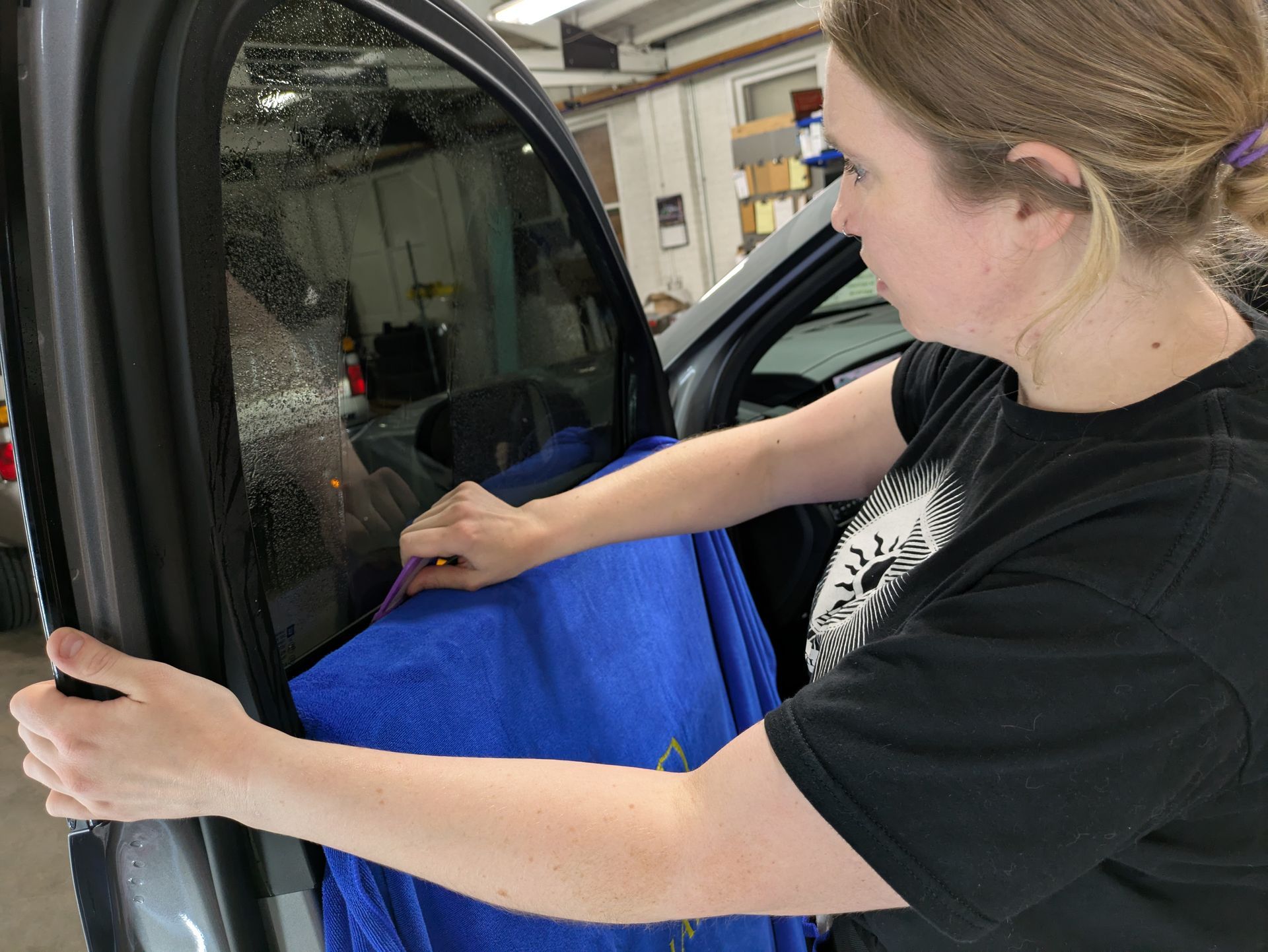 A woman is cleaning a car window with a blue towel.