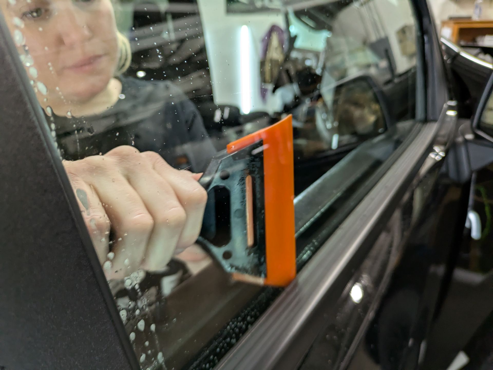 A woman is cleaning a car window with a squeegee.