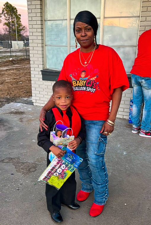 A woman in a red shirt is standing next to a boy in a black suit.