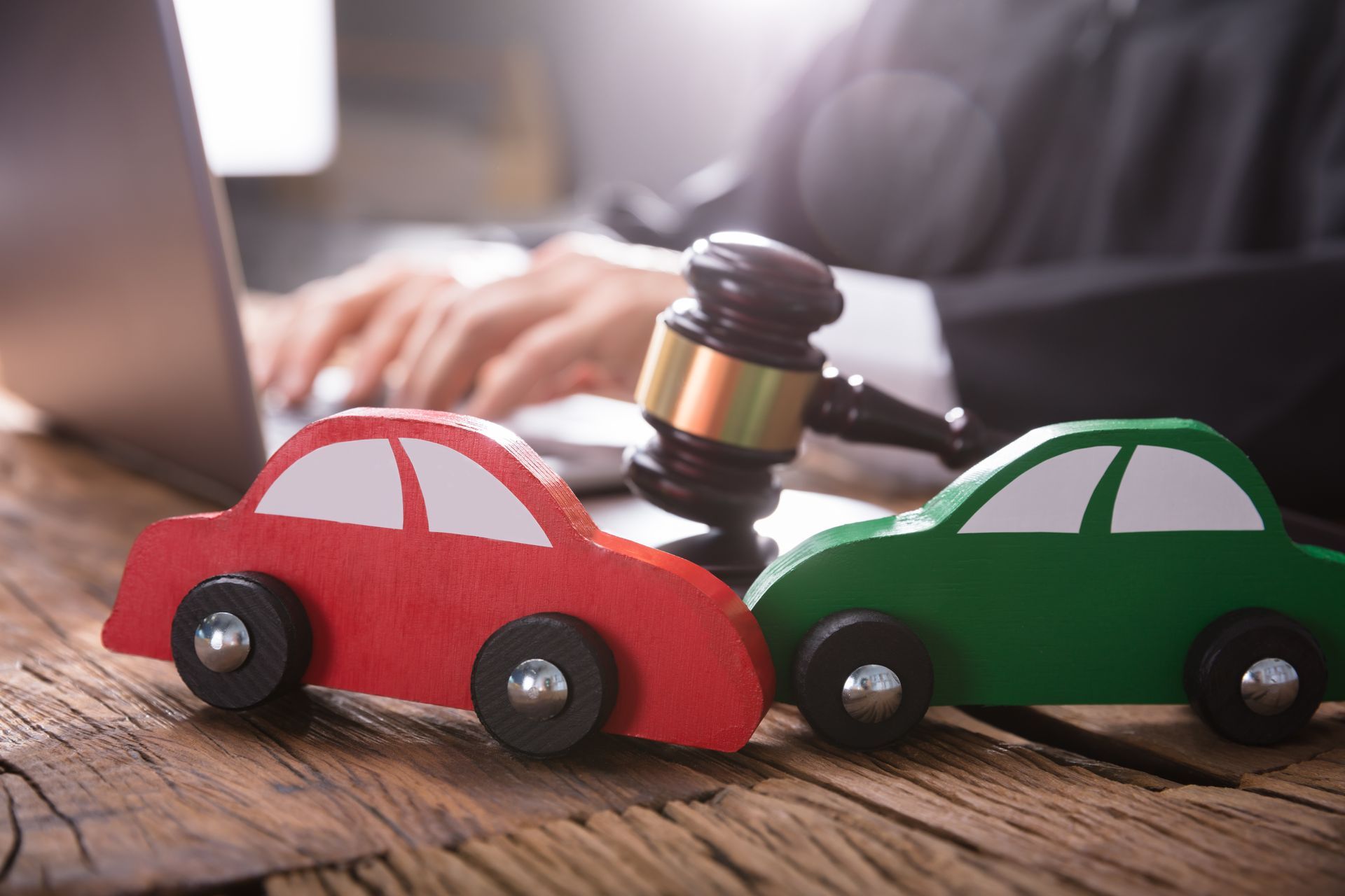 Two wooden cars are sitting on a wooden table next to a judge 's gavel.