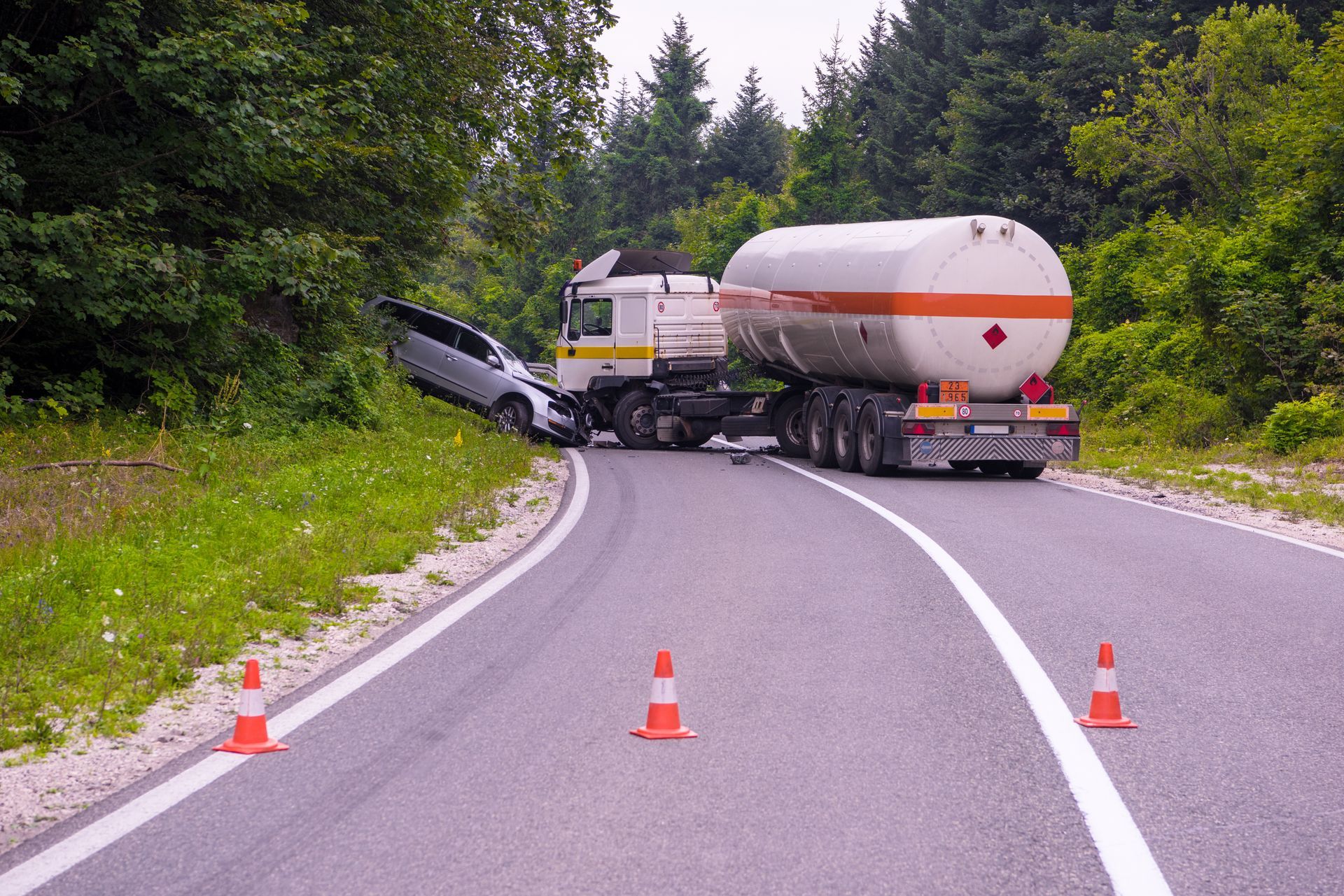 A car has crashed into a tanker truck on the side of the road.