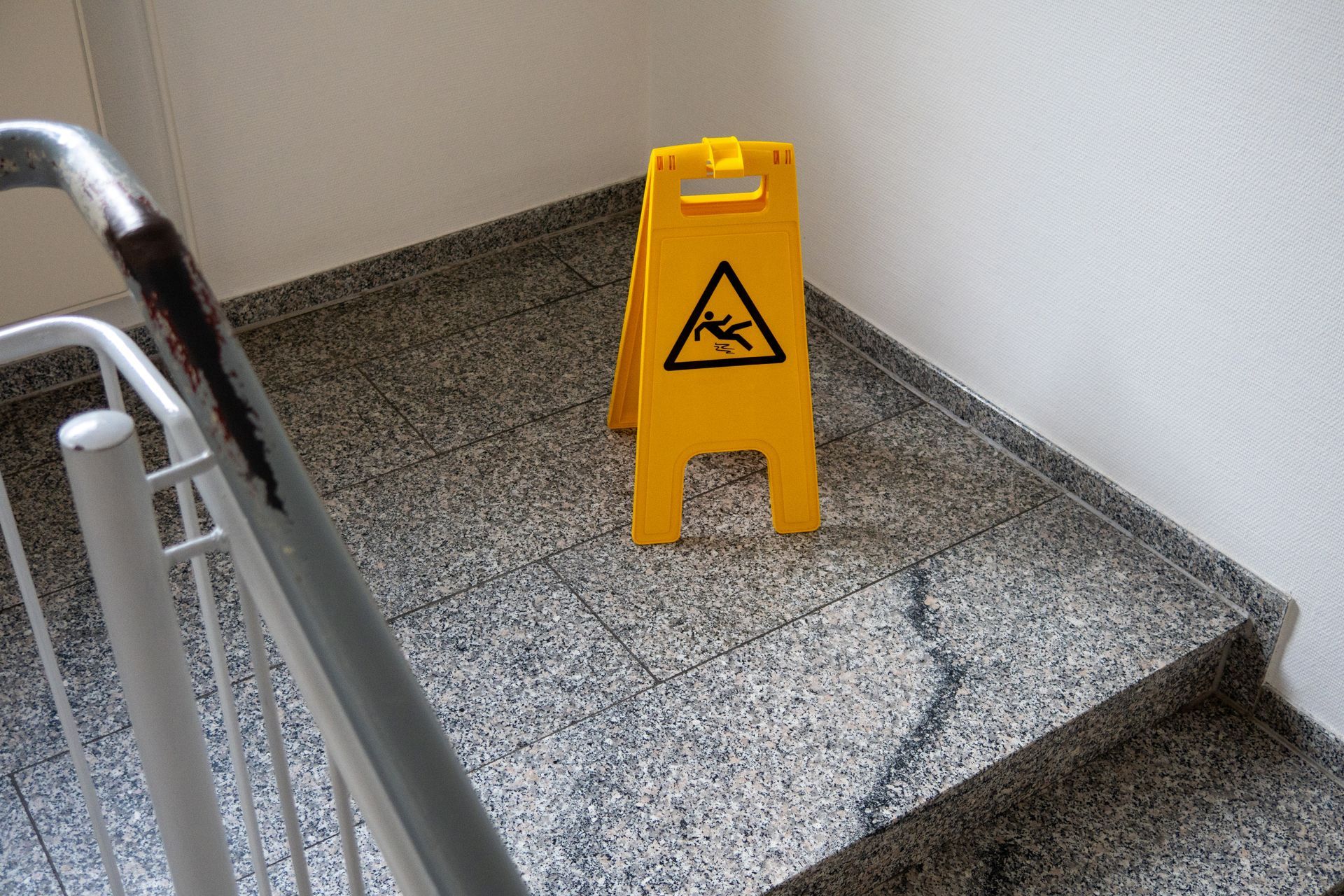 A yellow caution sign is sitting on the side of a set of stairs.