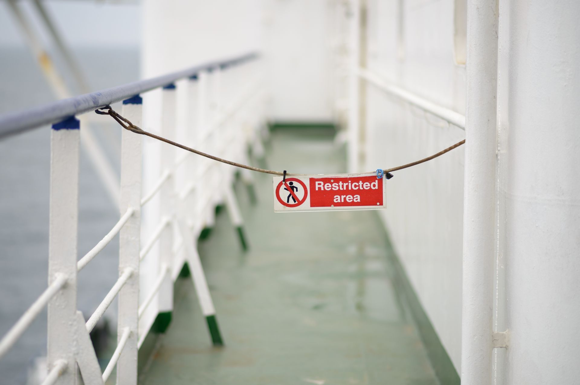 A red sign that says restricted area is hanging from a rope on a boat.