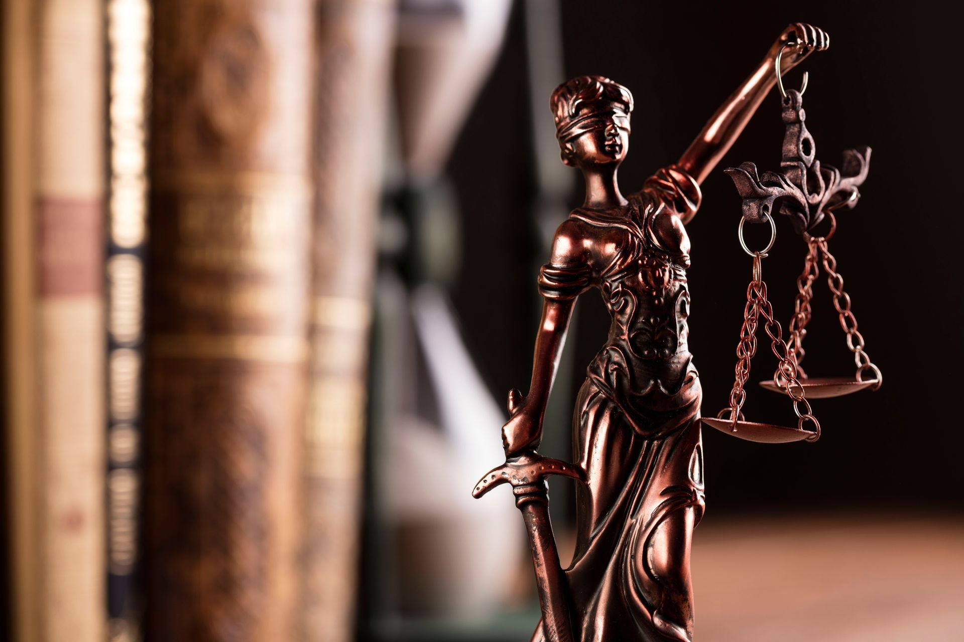 A statue of justice holding scales of justice in front of a book and hourglass.