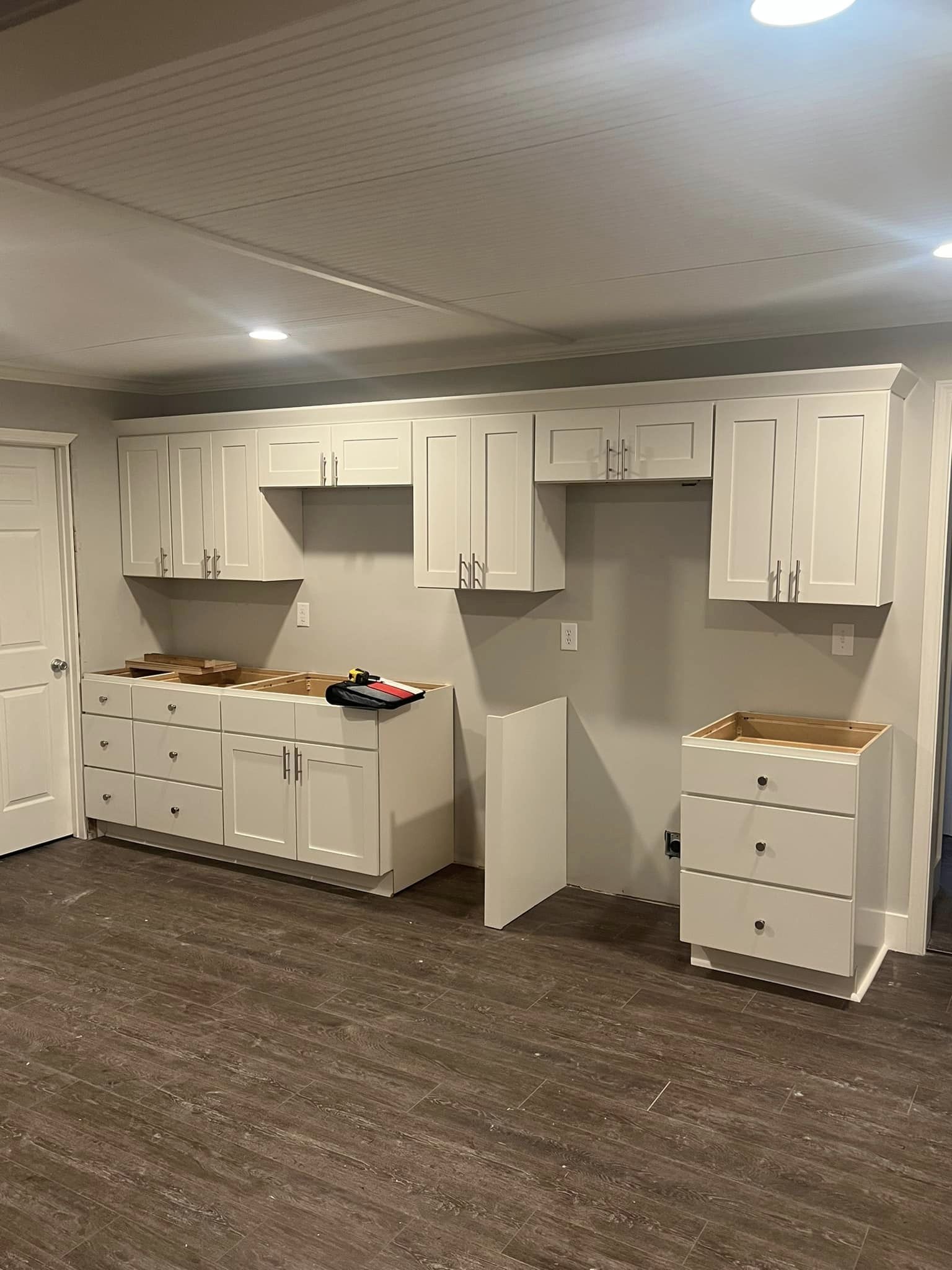 A kitchen in a basement with white cabinets and a brown carpet.