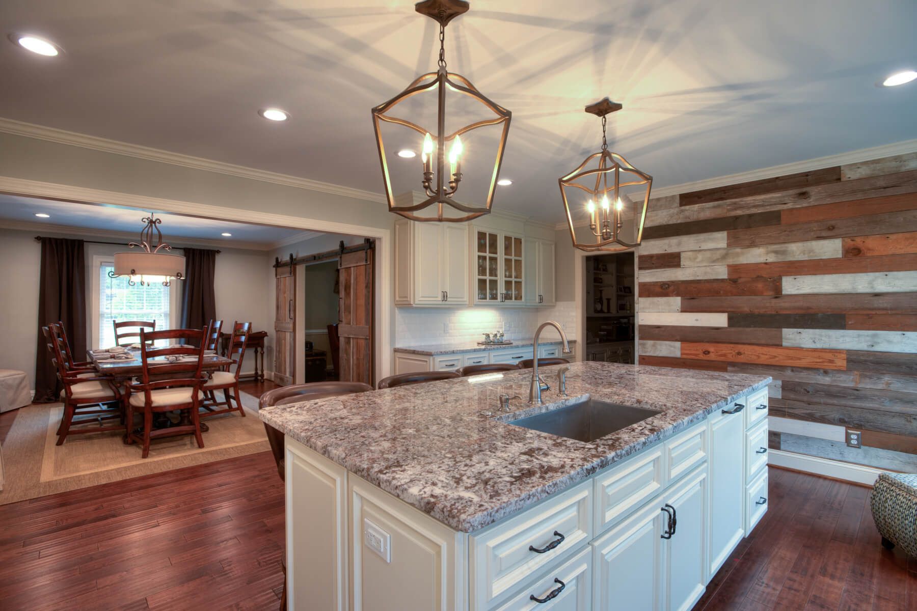 A kitchen with granite counter tops , white cabinets , a sink and a wooden wall.