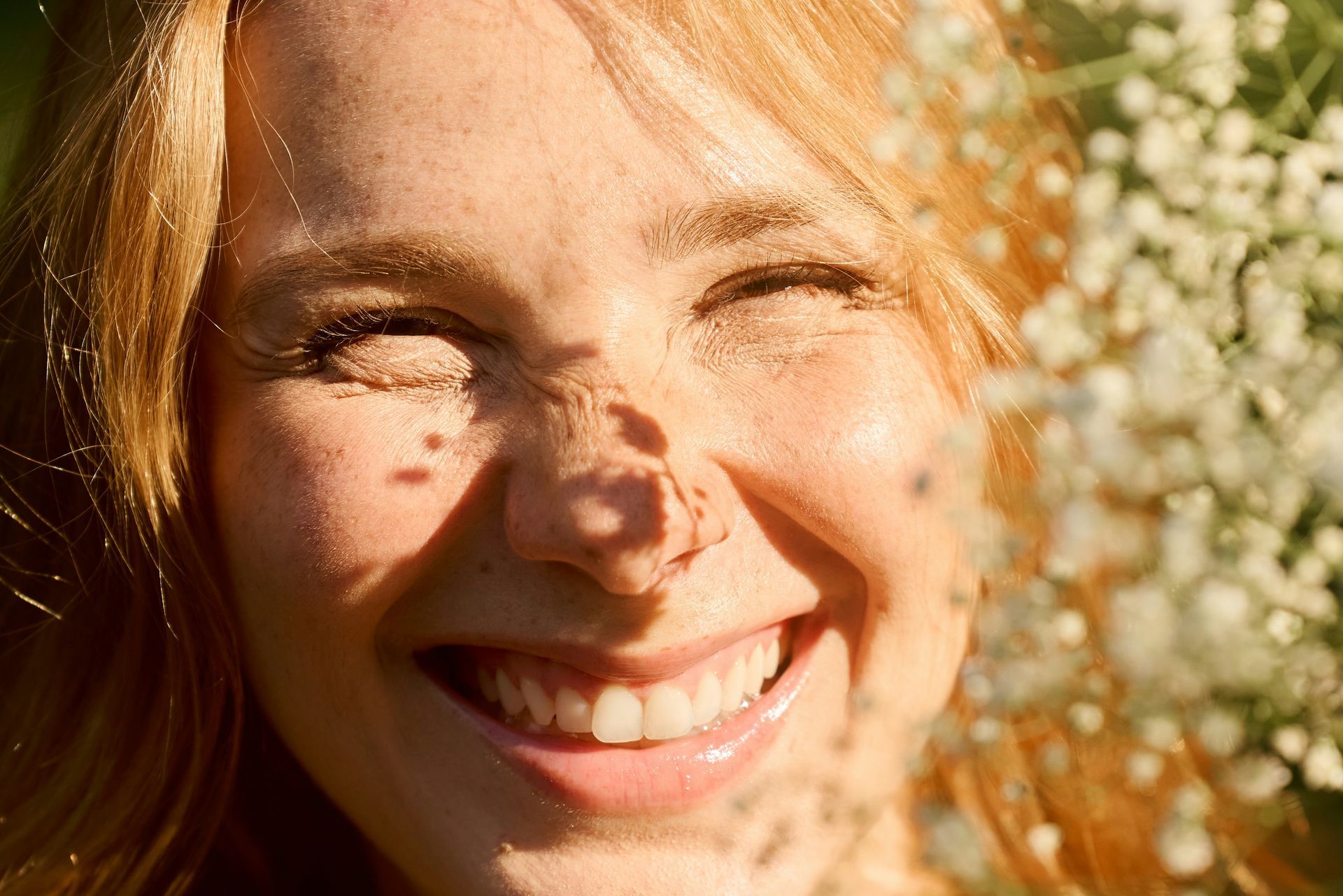 Joyful woman smiling in sunlight surrounded by flowers, capturing the confidence and lightness that can come from working with a top therapist in Sacramento.