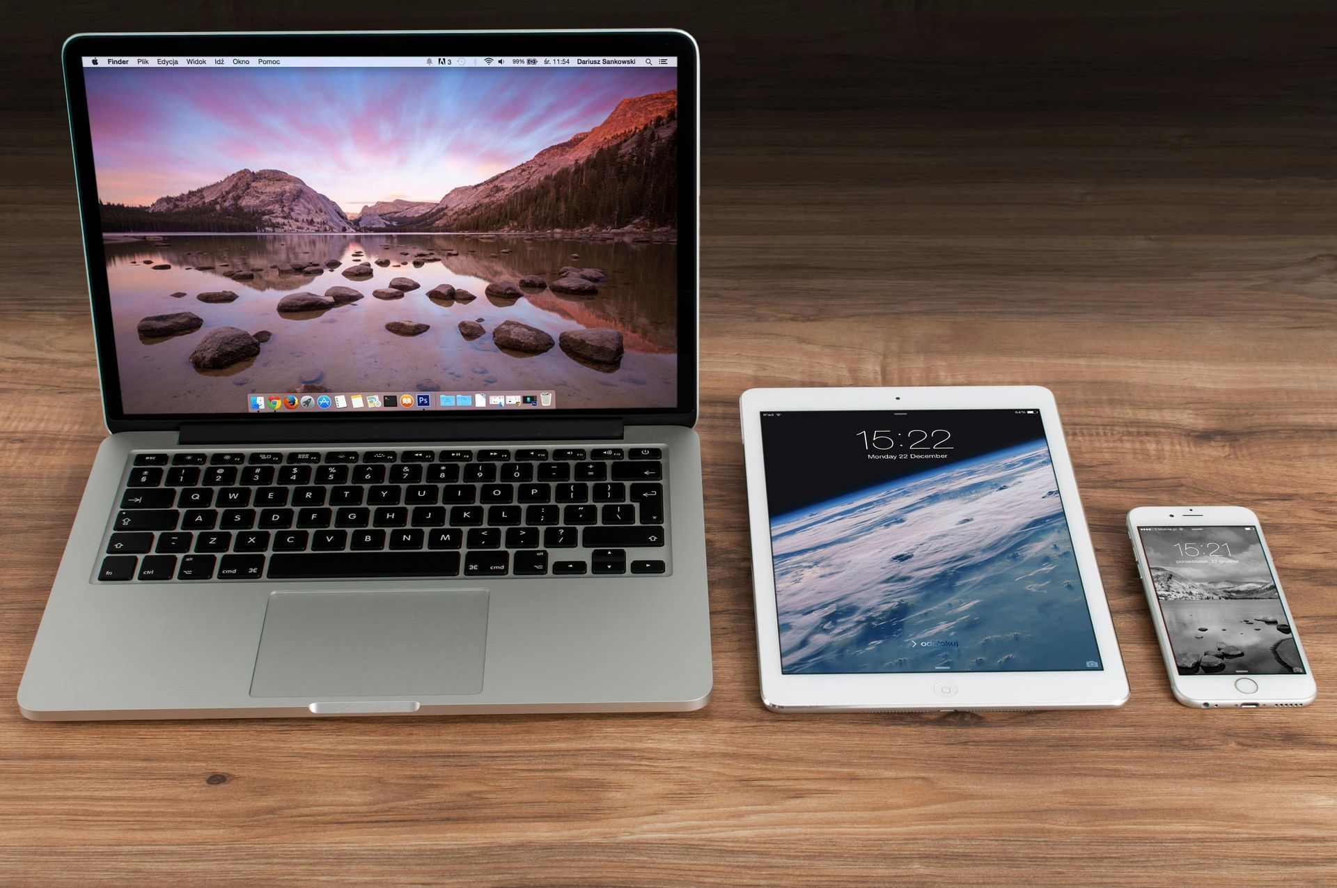 A laptop , tablet , and cell phone are on a wooden table.