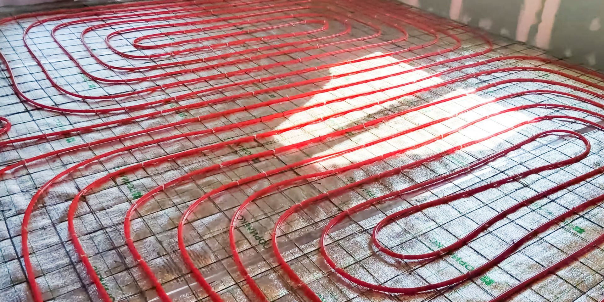 Red radiant floor heating tubing laid on a grid, ready for a concrete pour.