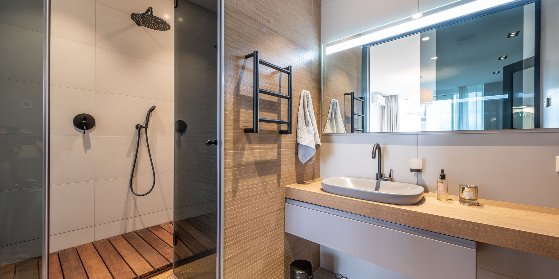 Modern bathroom with shower, vanity, and large mirror. Neutral tones, wooden accents, and black fixtures.
