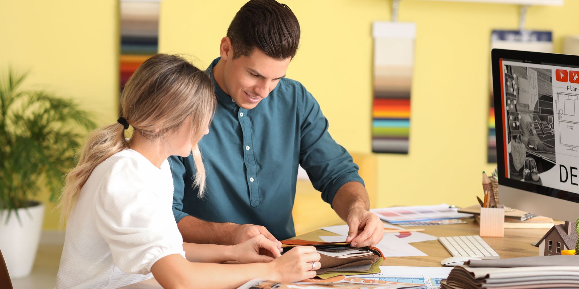 A man and woman examining a portfolio together at a desk with a computer and papers.