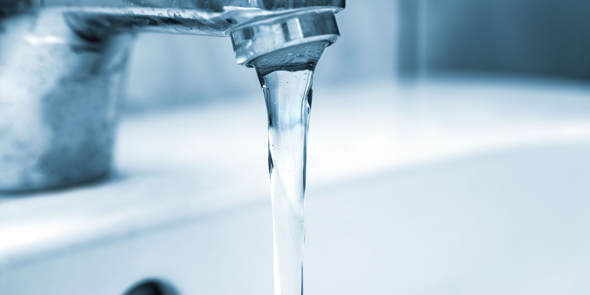 Close-up of a faucet with water flowing into a white sink. Blue tones dominate the scene.