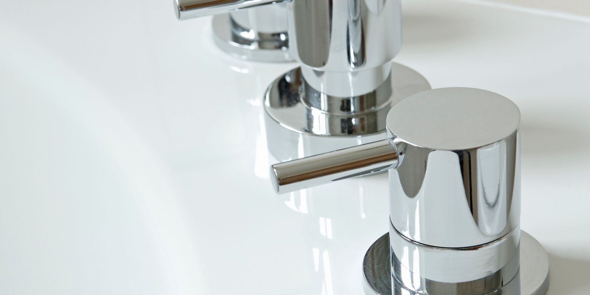 Close-up of three shiny, chrome faucet handles on a white surface.