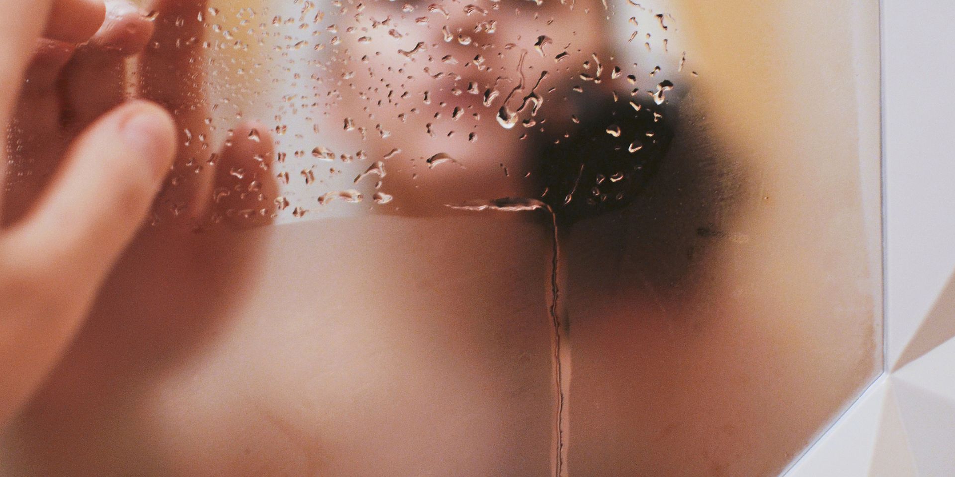 A person is taking a shower and looking at their reflection in the mirror.