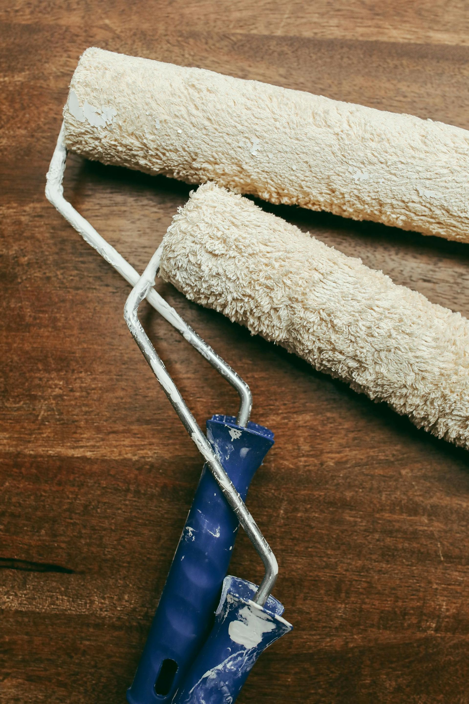 Two paint rollers with blue handles are sitting on a wooden table.