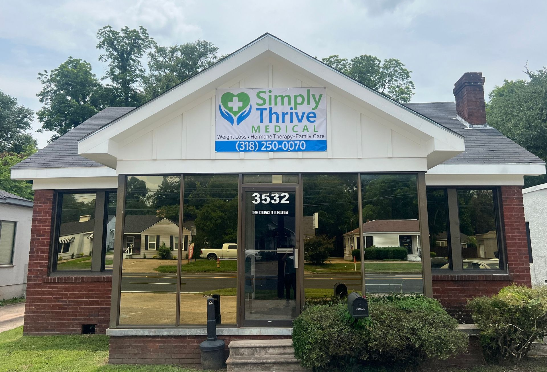 Simply Thrive Medical office building with glass windows, a blue sign, and red brick exterior.